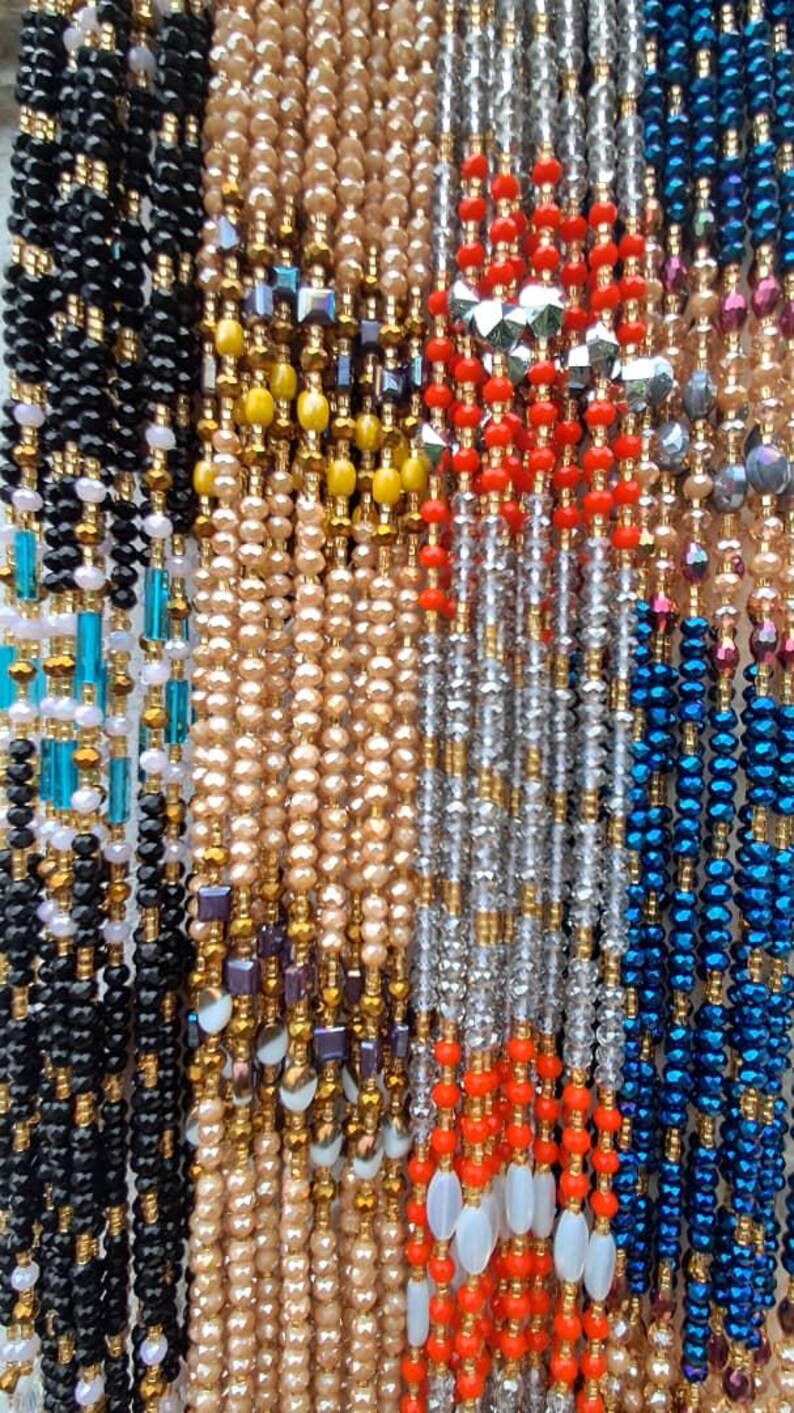 Puede incluir: Una colecci&oacute;n de collares de cuentas de varios colores, incluyendo negro, dorado, blanco, rojo, azul y turquesa. Las cuentas est&aacute;n dispuestas en filas verticales, creando un patr&oacute;n colorido y texturizado.