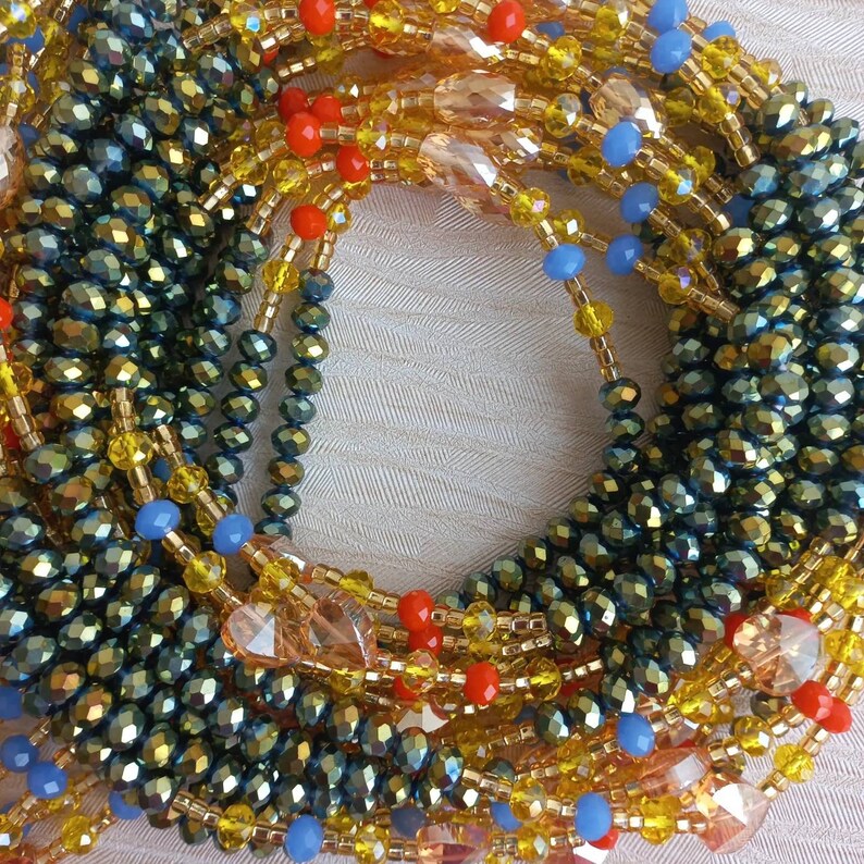 Puede incluir: Primer plano de un collar de cuentas multicadena con cuentas de color verde oscuro, dorado, naranja y azul. El collar est&aacute; hecho de cuentas de varios tama&ntilde;os y formas, creando un aspecto texturizado y en capas.