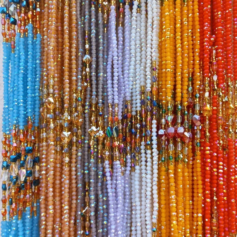 Puede incluir: Primer plano de una variedad de collares de cuentas de diferentes colores, incluyendo azul, naranja, blanco y rojo. Las cuentas est&aacute;n todas enhebradas en hilo dorado.