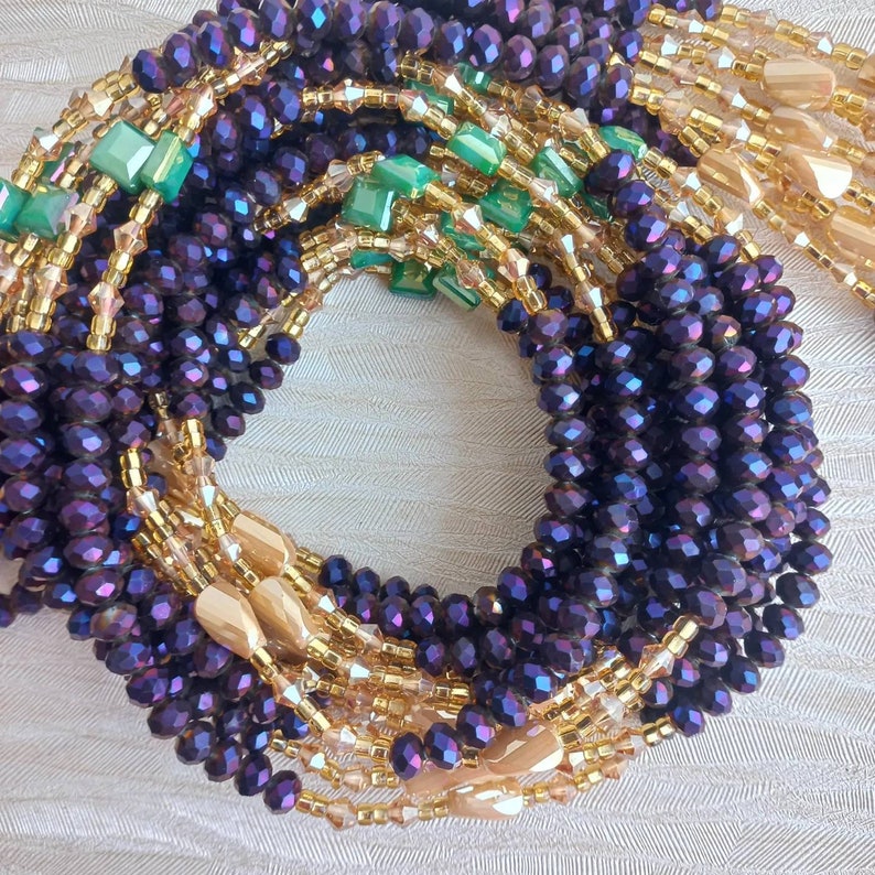 Puede incluir: Un collar de cuentas de cintura hecho de m&uacute;ltiples hilos de cuentas. Las cuentas son una mezcla de morado oscuro, dorado y verde.
