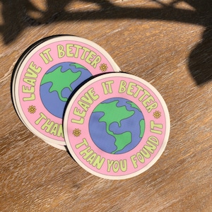 May include: Two pink and white round stickers with the text "Leave it better than you found it" and a cartoon image of the Earth. The stickers have yellow flowers around the text.
