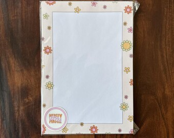 May include: A white notepad with a floral border. The notepad has a pink circle with the text "Mercy, Mercy Me Maggie" in white.