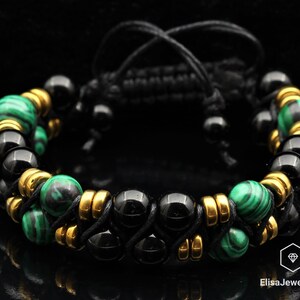 May include: A black and green beaded bracelet with gold accents. The bracelet is made with black onyx, malachite, and gold beads. The bracelet is adjustable with a black cord.