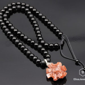 May include: A black onyx beaded necklace with a red crystal pendant. The necklace has a black cord with a sliding knot for adjusting the length. The pendant is a cluster of red crystals.