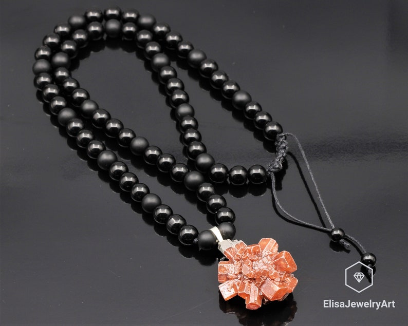 May include: A black onyx beaded necklace with a red crystal pendant. The necklace has a black cord with a sliding knot for adjusting the length. The pendant is a cluster of red crystals.