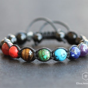 May include: A black cord bracelet with seven round gemstone beads in the colors of the rainbow. The beads are red, orange, yellow, green, blue, indigo, and violet.