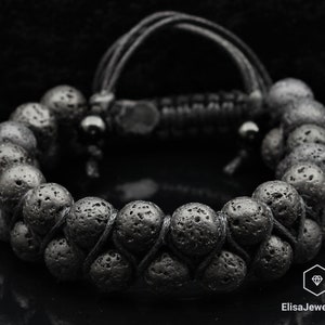 Op de afbeelding: Zwarte lavastenen armband met een zwart gevlochten koord. De armband is dubbel gelaagd en heeft een textuur.