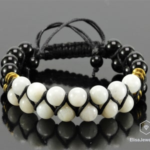 May include: Black and white beaded bracelet with a black cord and gold accents. The bracelet features round white beads and black beads.