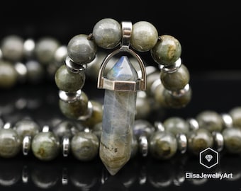 May include: A silver pendant with a faceted, gray labradorite crystal hangs from a gray beaded necklace. The pendant is shaped like a teardrop and has a silver loop at the top.