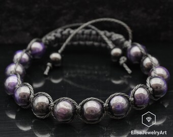 May include: A black cord bracelet with purple and black beads. The bracelet is tied with a knot and has a decorative knot at the end.