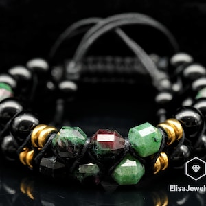 May include: A black and green gemstone bracelet with gold accents. The bracelet is made with black beads and green and red gemstones.