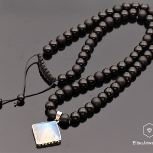 May include: A black onyx beaded necklace with a silver pendant featuring a square iridescent stone. The necklace has a black cord with a sliding knot for adjusting the length.