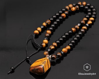 May include: A necklace with a large tiger's eye pendant and black and brown beads. The necklace has a black cord with a sliding knot for adjusting the length.