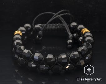 May include: Black beaded bracelet with gold accents. The bracelet is made of black beads and has a gold clasp. The bracelet is tied with a black cord.