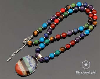 Può includere: Una collana di pietre preziose multicolori con un grande ciondolo ovale. La collana presenta perline di pietre preziose rosse, arancioni, gialle, verdi, blu, indaco e viola. Il ciondolo è realizzato con pietre preziose stratificate degli stessi colori delle perline. La collana ha una chiusura argentata.