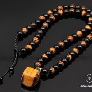 May include: A necklace made with black and tiger's eye beads. The necklace has a pendant made of a large tiger's eye stone.
