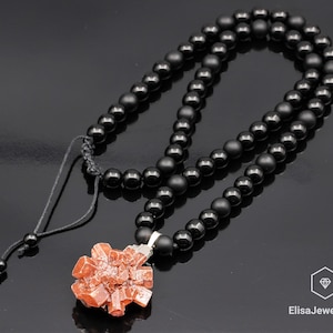 May include: A black beaded necklace with a red crystal pendant. The necklace is made of black onyx beads and has a simple adjustable clasp. The pendant is a cluster of red crystals.