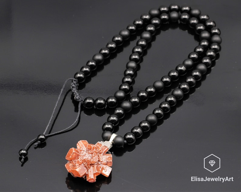 May include: A black beaded necklace with a red crystal pendant. The necklace is made of black onyx beads and has a simple adjustable clasp. The pendant is a cluster of red crystals.