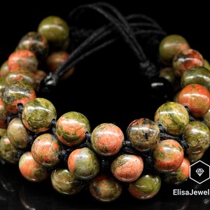 May include: A bracelet made of green and red jasper beads strung on black cord. The bracelet is adjustable and has a knotted design.