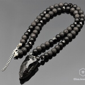 May include: Black beaded necklace featuring a black obsidian arrowhead pendant. The necklace is crafted with black lava rock and onyx beads.