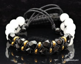 May include: Black and white beaded bracelet with gold accents. The bracelet is made with black faceted beads, white round beads, and gold spacer beads. The bracelet is tied with a black cord.