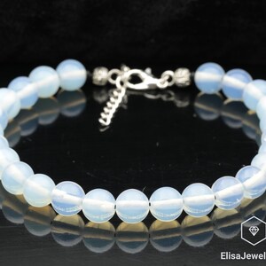 Pode incluir: Um bracelete de contas de opala branca com um fecho prateado. O bracelete é feito de contas redondas e lisas e tem um visual delicado e feminino.