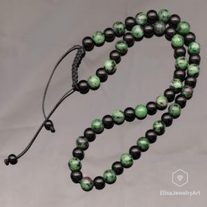 May include: A beaded bracelet featuring alternating round black beads and mottled green and black zoisite beads. The bracelet includes a black cord with an adjustable sliding knot closure and two small black beads at the ends of the cords.