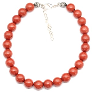 May include: A red gemstone beaded necklace with silver clasps. The necklace is made of round beads and has a simple design.