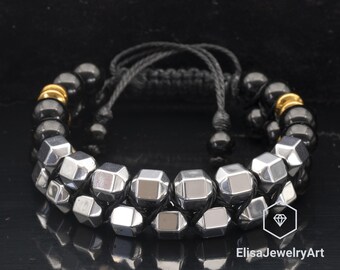 May include: A black and silver bracelet with a braided cord and gold accents. The bracelet features a double row of faceted, geometric beads.