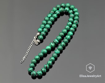 May include: A green malachite beaded necklace with a silver clasp. The beads are round and have a swirling pattern.