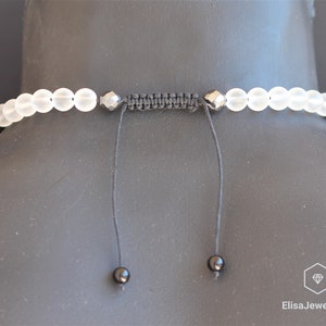 May include: A white frosted bead necklace with black accents and a black cord closure. The necklace is adjustable and has a simple design.