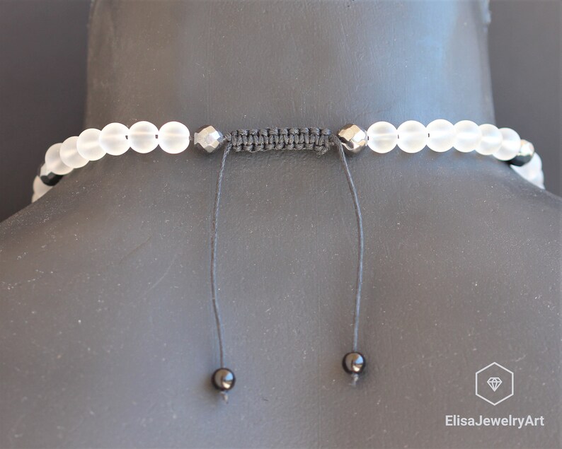 May include: A white frosted bead necklace with black accents and a black cord closure. The necklace is adjustable and has a simple design.