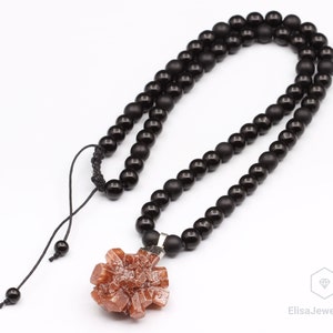 May include: A black beaded necklace with a brown crystal pendant. The necklace has a black cord with a knot at the top.