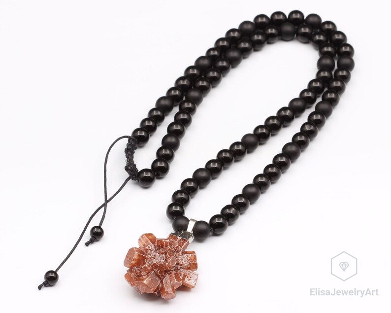 May include: A black beaded necklace with a brown crystal pendant. The necklace has a black cord with a knot at the top.