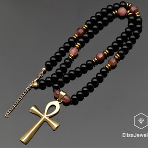 May include: A gold ankh pendant necklace with black and pink beads. The necklace is made of black onyx and rose quartz beads.