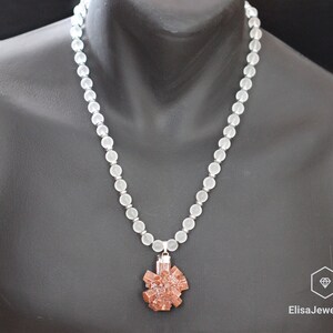 May include: A white frosted bead necklace with a brown crystal pendant. The pendant is a cluster of crystals in a starburst shape.