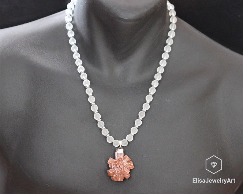May include: A white frosted bead necklace with a brown crystal pendant. The pendant is a cluster of crystals in a starburst shape.