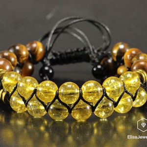May include: A double-strand bracelet with yellow and brown beads. The bracelet is made with a black cord and has a knot closure.