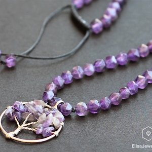 May include: A purple amethyst gemstone necklace with a wire-wrapped tree pendant. The necklace is made with faceted amethyst beads and a silver chain. The pendant features a tree design with small amethyst stones.