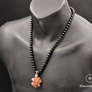 May include: A black beaded necklace with a pendant featuring a cluster of orange-brown crystals. The necklace is on a black mannequin.