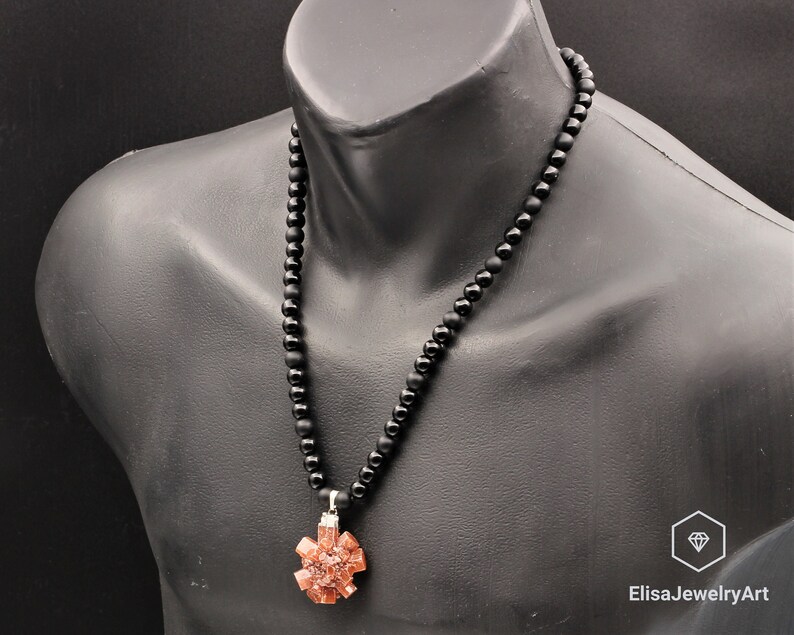 May include: A black beaded necklace with a pendant featuring a cluster of orange-brown crystals. The necklace is on a black mannequin.
