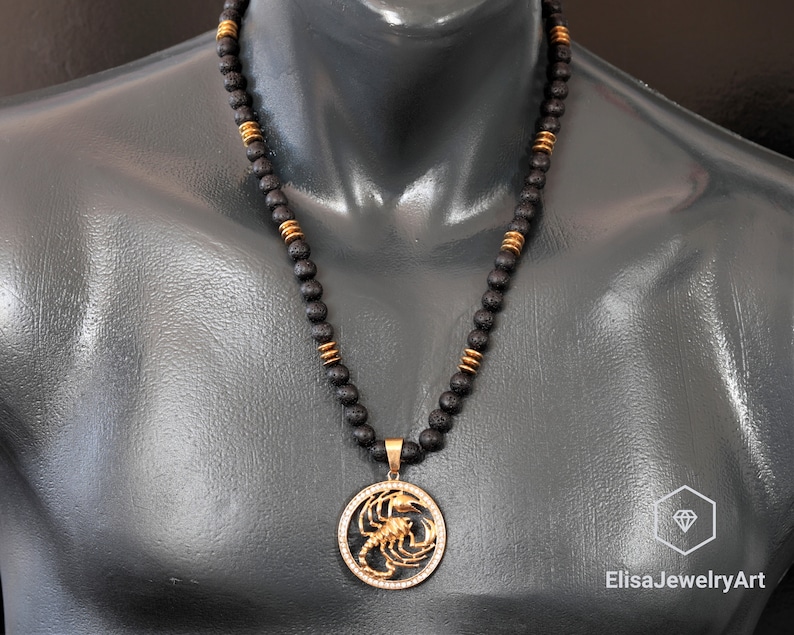 Op de afbeelding: Een zwarte lavastenen kralenketting met een gouden hanger in de vorm van een schorpioen. De hanger is omringd door heldere strass steentjes.
