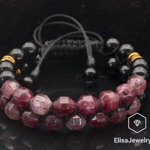 May include: A black cord bracelet with pink and red gemstone beads. The bracelet has gold accents and is tied with a knot.
