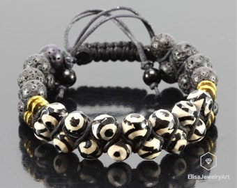 May include: Black and white patterned beads with gold accents are strung on a black cord with black lava rock beads. The bracelet has a sliding knot closure.