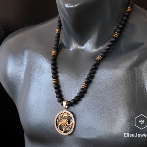 Op de afbeelding: Een zwarte kralenketting met een gouden hanger met een schorpioenontwerp. De ketting is om de nek van een mannequin.