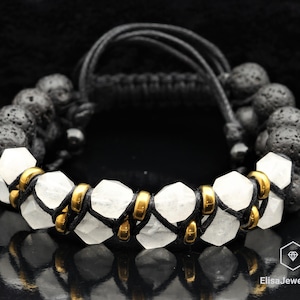 May include: A black lava rock and white crystal beaded bracelet with gold accents. The bracelet is made with a black cord and has a knotted design.