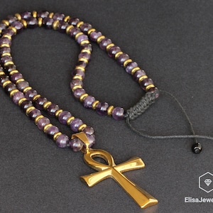 May include: A gold ankh pendant necklace with a double strand of amethyst beads and a black cord with a sliding knot.