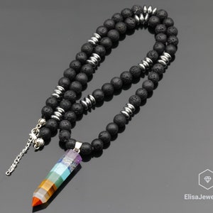 Könnte beinhalten: Eine schwarze Lava-Perlenkette mit silbernen Akzenten und einem mehrfarbigen Kristall-Anhänger. Der Anhänger ist ein sieben-Chakra-Stein mit den Farben Rot, Orange, Gelb, Grün, Blau, Indigo und Violett.