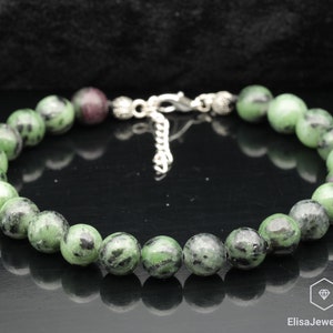 Może przedstawiać: Bransoletka z zielonych i czarnych kamieni szlachetnych z srebrnymi akcentami. Bransoletka wykonana jest z okrągłych koralików i ma zapięcie.