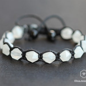 May include: A white gemstone bracelet with a black cord. The bracelet is made with faceted gemstones and has a simple design.